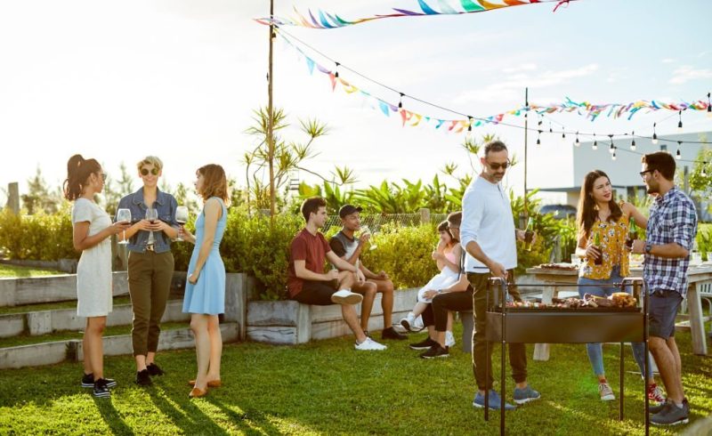 Family and friends enjoying Asado party on sunny day. Males and females are spending leisure time together. They are in backyard during summer.