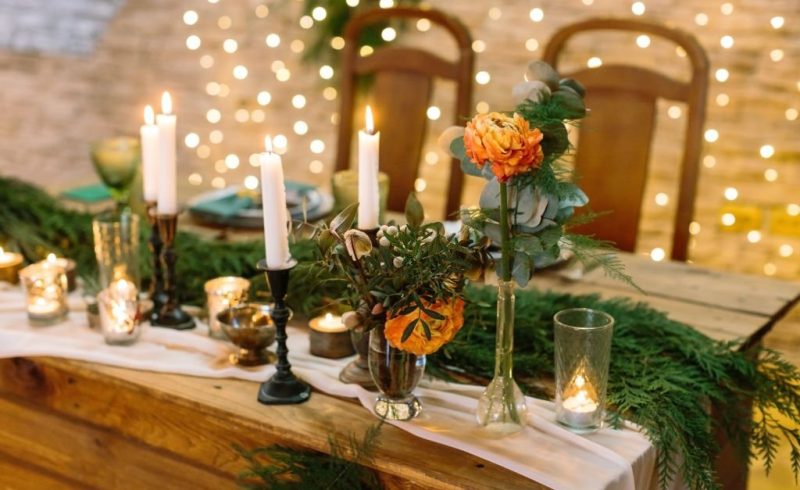 christmas, celebration, design concept. close up of delicate flower, bud of rose in tender orange colour, it is surrounded by lots of candles and leghts, glasses and fuzzy branches of spruce