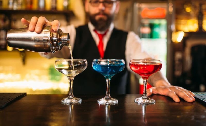 Bartender with shaker making alcohol beverages behind a bar counter in nightclub