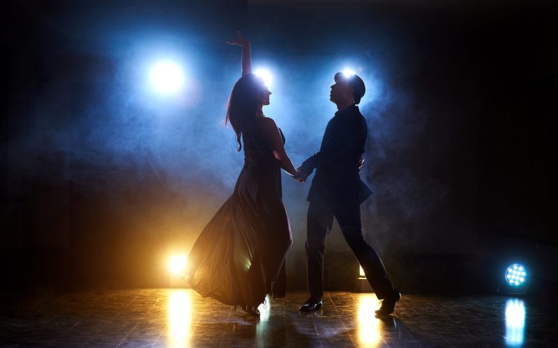 Skillful dancers performing in the dark room under the concert light and smoke. Sensual couple performing an artistic and emotional contemporary dance.